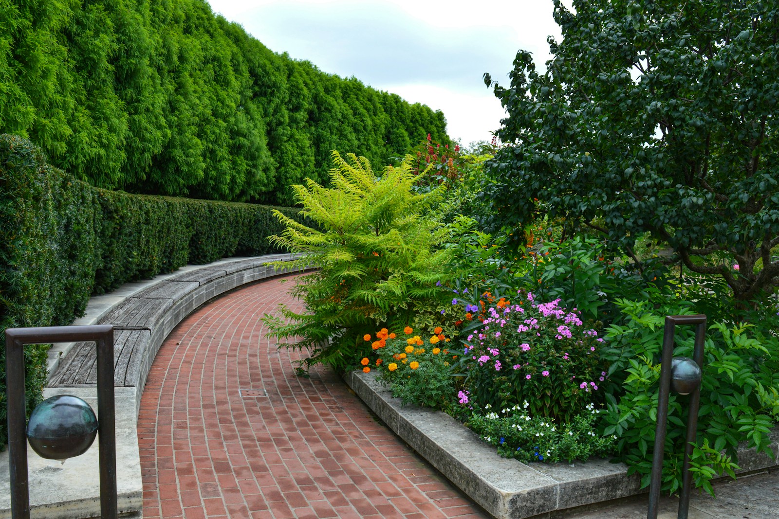 Curved brick pathway winds through a lush garden, featuring vibrant flowers and greenery, creating a serene outdoor space for relaxation.